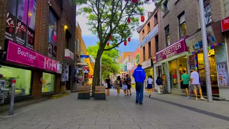 Tiendas-Minoristas-Bilingües-Chinas-Francesas-En-Una-Calle-Peatonal-Tarde-De-Verano-En-Montreal,-Canadá,-Donde-Los-Turistas-Compran-Tranquilamente-Interactuando-Con-Personas-Locales-Desnutridas-Y-Con-Problemas-De-Pobreza.