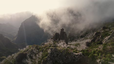 Drone-flying-in-the-mountains-at-Madeira-between-rugged-steep-rocks-and-misty-ridgelines-during-sunrise