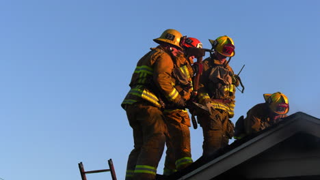 Bomberos-En-El-Techo,-Abriéndose-Camino-Dentro-De-Una-Casa-Humeante,-Tarde-Soleada.