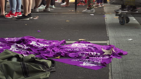 Primer-Plano-De-Pañuelos-Políticos-Feministas-Morados-A-La-Venta-En-Una-Manifestación-Sobre-El-Aborto,-La-Gente-Marcha-Junto-A-Ellos