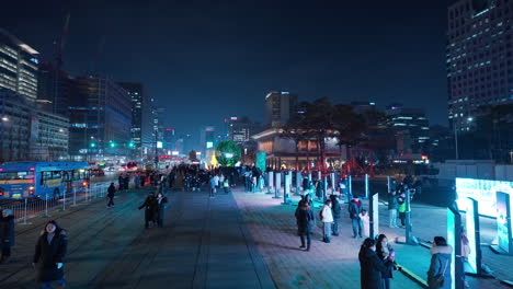 La-Gente-Viaja-A-La-Plaza-Gwanghwamun-Viendo-La-Galería-De-Arte-Al-Aire-Libre-En-Grandes-Pantallas-LED-Con-El-Horizonte-Nocturno-De-La-Ciudad-De-Seúl---Vista-Elevada