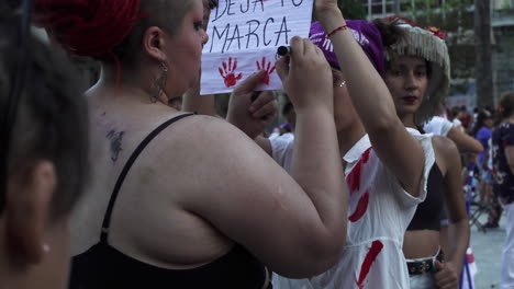 Two-female-protesters-with-sign,-have-red-stains-that-imitate-blood,-perform-public-demonstration-of-discontent