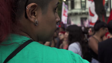 Primer-Plano-De-La-Espalda-De-Una-Joven-Defensora-Durante-Una-Protesta-Pacífica,-Vestida-Con-Ropa-Verde-Y-Aretes-Con-El-Pelo-Rojo