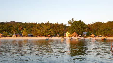 Scenic-coastal-landscape-with-people-on-white-sandy-beach-with-rainforest-trees-on-West-Papuan-tropical-island,-Indonesia