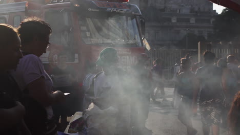 Atmósfera-Con-Humo-En-Un-Evento-Público-Donde-Está-Estacionado-Un-Vehículo-De-Bomberos,-La-Gente-Camina-En-Todas-Direcciones