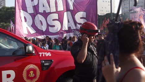 Bombero-Con-Su-Auto-De-Bomberos-Estacionado-Camina,-Se-Comunica-Con-Teléfono-En-Manifestación-Pública,-Responde-A-Llamada-De-Emergencia