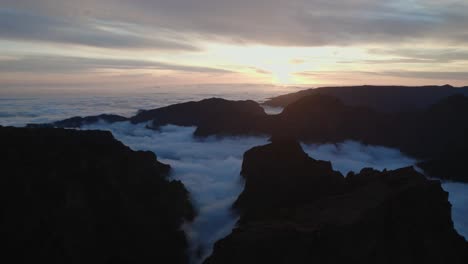 Drone-flying-over-the-clouds-at-sunset-at-Pico-Do-Arieiro,-Madeira-through-mountains