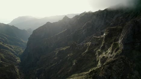 Drone-flying-in-the-mountains-at-Madeira-between-rugged-steep-rocks-and-misty-ridgelines-during-sunrise