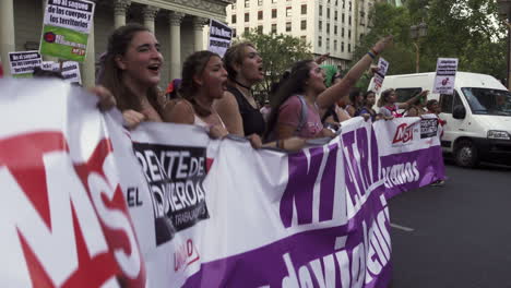 Mujeres-Jóvenes-Manifestantes-Marchan-Y-Cantan-Por-Sus-Derechos-Con-Tambores-Y-Una-Pancarta-Morada-Alrededor-De-La-Plaza-De-Mayo-Y-La-Catedral,-Sostienen-Carteles-De-Protesta-Feminista.