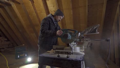 Hombre-Con-Gorro-Usando-Una-Sierra-Ingletadora-En-Un-Taller-De-Carpintería,-Aserrín,-Artesanía-Enfocada,-Iluminación-Interior