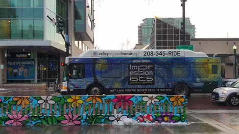 Main-Street-view-with-public-transport-bus-and-traffic-driving-in-light-snow-during-cold-winter-fall-season-day-in-downtown-city