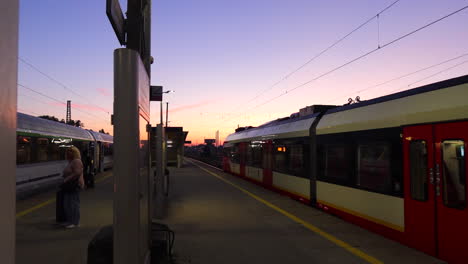 Early-morning-pink-sunrise-and-people-walking-near-two-trains-at-the-Warsaw-East-Station-in-Poland,-Warszawa-Wschodnia-train-station,-4K-static-shot