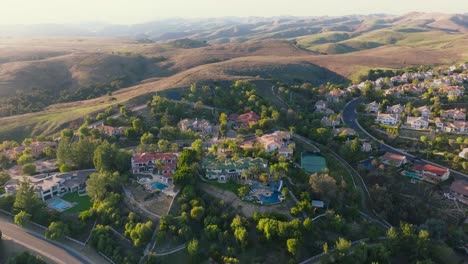 Dream-Homes-Nestled-in-Sunlit-Hills-of-Calabasas,-Sunset-and-Mountains-on-Horizon,-Luxury-Mansions-Below