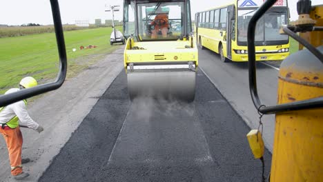 Road-construction-worker-operating-a-yellow-roller-on-fresh-asphalt,-view-from-another-vehicle-near-Buenos-aires