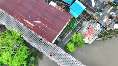 Indonesian-people-crossing-wooden-bridge,-remote-rural-village,-wooden-huts