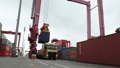 Container-being-lifted-by-crane-above-truck-at-commercial-port,-daylight-at-port-of-Buenos-Aires