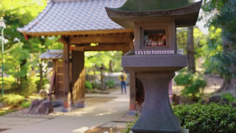 Panorámica-En-Cámara-Lenta-Estableciendo-Una-Toma-De-Las-Puertas-Del-Templo-Y-Una-Linterna-De-Piedra-Con-Gatos-Afortunados-En-Gotokuji