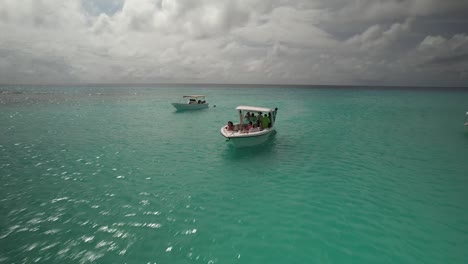 Turquoise-waters-with-boats-and-swimmers-at-Los-Roques,-Venezuela,-on-a-sunny-day,-aerial-view