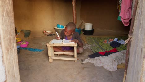 Vista-Frontal-De-Un-Joven-Dedicado-A-Estudiar-A-La-Luz-Del-Día-En-Su-Tradicional-Casa-De-Barro-En-La-Aldea-De-Wulugu,-Ghana