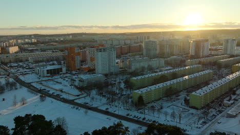 Golden-hour-over-a-snow-clad-urban-landscape-featuring-a-standout-orange-building-amidst-uniformly-colored-apartments,-reflecting-the-fading-sunlight---Gdańsk