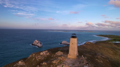 Old-lighthouse-on-a-coastal-hillside-in-Venezuela,-overlooking-the-Caribbean-Sea-at-dusk,-aerial-view