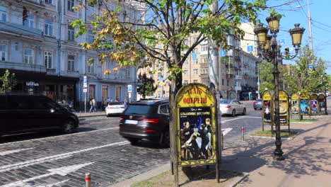 Beautiful-sunny-Kyiv-city-center-street-with-cars-driving-on-the-road-and-apartment-buildings-in-Ukraine,-trees-and-lamps,-people-walking,-4K-shot