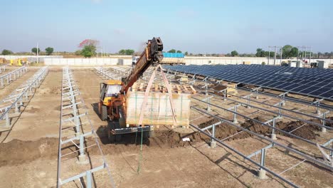 AERIAL-DRONE-VIEW-DRONE-CAMERA-GOING-TO-THE-BACK-SIDE-WHERE-JCB-IS-PICKING-UP-A-BOX-OF-SOLAR-PANELS