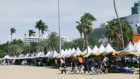 Eine-Gruppe-Von-Touristen,-Die-Auf-Der-Rechten-Seite-Des-Bildes-Vor-Zelten-An-Der-Küste-Von-Pattaya-In-Der-Provinz-Chonburi-In-Thailand-Spazieren