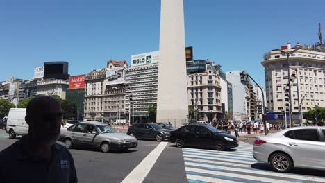 Car-traffic-on-sunny-9-de-Julio-Avenue-in-summer,-obelisk-skyline-center-of-Town