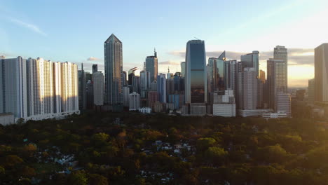 Manila-South-Cemetery-and-the-sunlit-Makati-cityscape,-in-Philippines---Ascending,-drone-shot