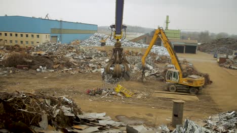 Klauenkran-Auf-Einem-Schrottplatz,-Der-Metallschutt-Hebt,-Bewölkter-Tag