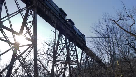 Norfolk-Southern-Train-with-Empty-Intermodal-Cars-Crosses-the-Pope-Lick-Trestle-in-Louisville,-KY,-as-the-Sun-Sets-in-the-Background