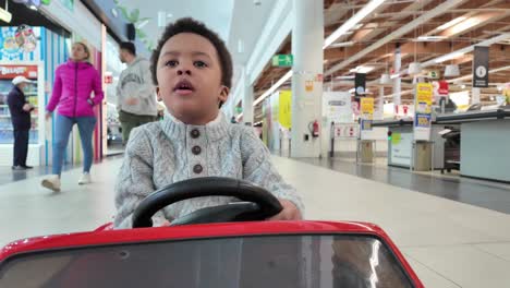 Adorable-Y-Divertido-Niño-Negro-De-3-Años-Montando-Un-Coche-De-Juguete-Eléctrico-Dentro-De-Un-Centro-Comercial.