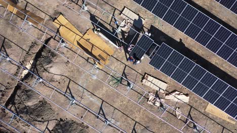 Aerial-drone-view-of-men-unboxing-and-fitting-solar-panels-and-lots-of-solar-panels-are-visible-around