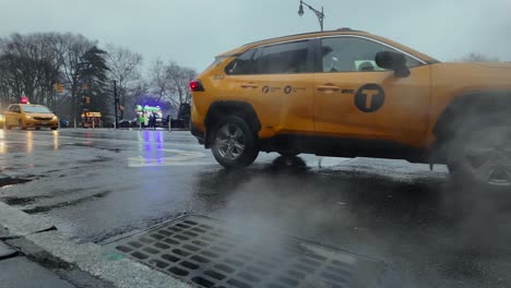 Una-Vista-De-ángulo-Bajo-De-Los-Taxis-Amarillos-De-Nueva-York-Conduciendo-Por-Un-Drenaje-De-Alcantarillado-Que-Emite-Vapor-En-Un-Día-Nublado-Y-Húmedo