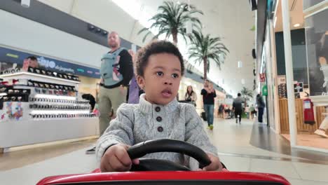 Lindo-Y-Exótico-Niño-Negro-De-3-Años-Montando-Un-Auto-De-Juguete-Eléctrico-Rojo-Dentro-De-Un-Centro-Comercial