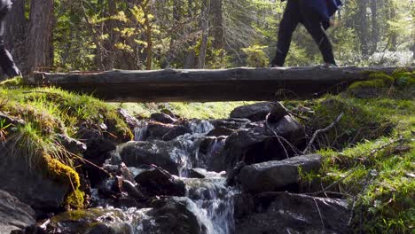 Wanderer-überqueren-Eine-Holzbrücke-über-Einen-Kleinen-Gebirgsbach,-Der-Ein-Steiniges-Bachbett-Hinunterfließt