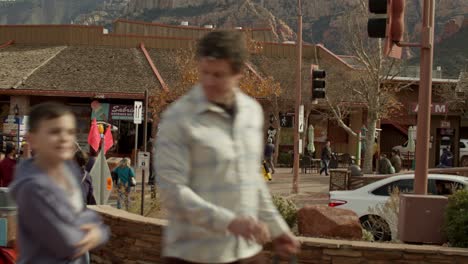 Butte-rock-formations-in-Sedona,-Arizona-with-camera-tilting-down-to-shoppers-in-downtown-Sedona,-Arizona