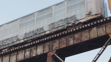 Ein-Mit-Graffiti-Bedeckter-Autotransporterzug-überquert-Bei-Sonnenuntergang-Einen-Alten,-Rostigen-Eisenbahnbock