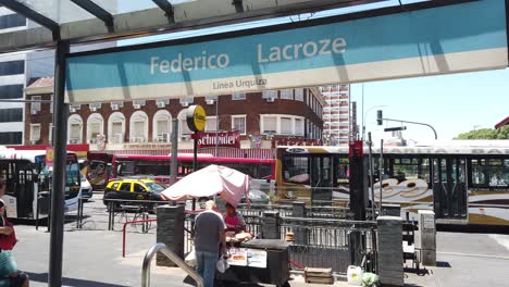 Vendedor-Ambulante-Vende-Panqueques-En-La-Estación-De-Tren-Federico-Lacroze-En-Chacarita,-Gente-De-Argentina-Caminando-Bajo-La-Luz-Del-Sol-En-Verano