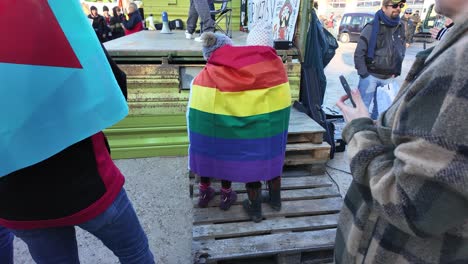 Dos-Niños-Se-Acurrucan-Con-La-Bandera-Del-Arco-Iris-Mientras-Hay-Una-Protesta-Contra-La-Extrema-Derecha-A-Su-Alrededor.