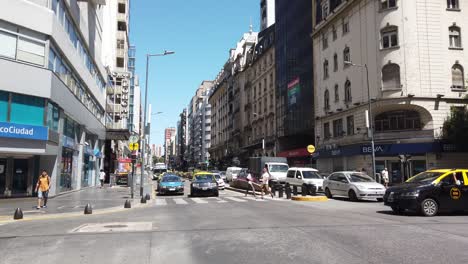 Panorámica-De-La-Avenida-Corrientes-Bajo-La-Luz-Del-Sol-Del-Verano-Calles-De-La-Ciudad-Tráfico-De-Automóviles-Peatones-Y-Horizonte-En-El-Famoso-Punto-Central