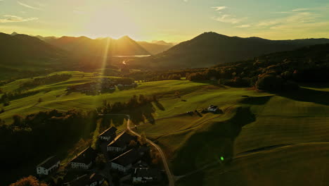 Beautiful-aerial-shot-of-the-sun's-rays-over-the-mountain-in-a-huge-green-field