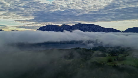 Beautiful-drone-shot-between-the-clouds-over-a-green-field-with-a-lake-and-some-small-houses