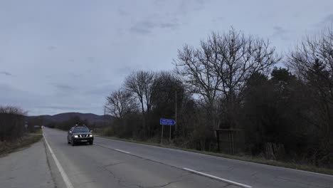 A-Nissan-pickup-truck-driving-on-the-E871-road-at-dusk,-passing-by-a-road-sign-for-the-Sarantsi-station