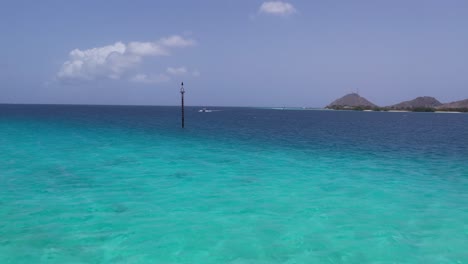 Crystal-clear-turquoise-waters-with-distant-hills-under-a-blue-sky-in-Los-Roques,-Venezuela,-serene-seascape