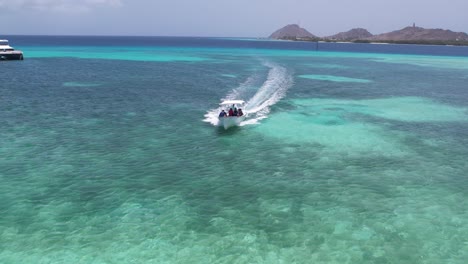 Lancha-Motora-Navegando-Por-Las-Cristalinas-Aguas-Azules-De-Los-Roques,-Venezuela,-Con-Pintorescas-Colinas-Al-Fondo,-Luz-Del-Día