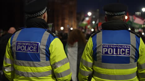 En-Cámara-Lenta,-Dos-Agentes-De-Policía-Metropolitanos-De-Inteligencia-Del-Orden-Público-Observan-Y-Monitorean-Una-Protesta-Nocturna-En-Las-Afueras-De-La-Abadía-De-Westminster.