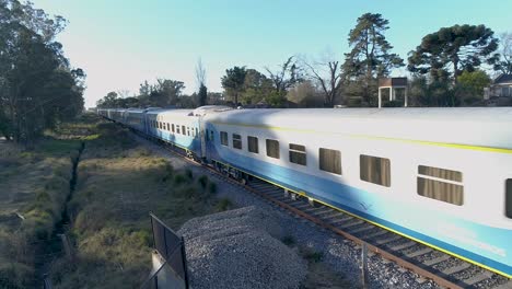 Trenes-De-Pasajeros-Con-Muchos-Vagones-Circulan-Por-Vías-Detrás-De-Casas-En-El-Campo.