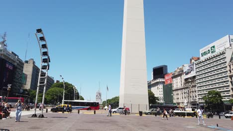 La-Gente-Camina-Alrededor-Del-Obelisco-En-El-9-De-Julio,-Los-Turistas-Del-Centro-De-La-Ciudad-De-La-Avenida-Corrientes-Disfrutan-De-La-Ubicación-De-La-Calle-De-Viajes-En-El-Centro,-El-Tráfico-Que-Pasa